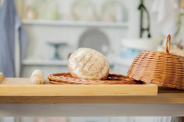 Хлеб возле плетеной корзины на столе в деревенской кухне. Комп — стоковое фото