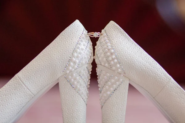 Um par de sapatos de casamento brancos com anéis em um banquinho — Fotografia de Stock