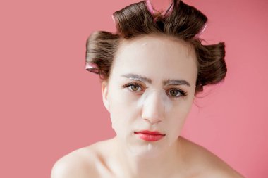Yüzüne dokunmadan bir maske ve curlers ile güzel genç kız.