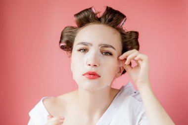 Yüzüne dokunmadan bir maske ve curlers ile güzel genç kız.