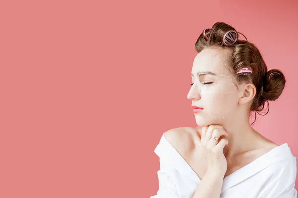 Menina bonita com uma máscara e curlers tocando seu rosto . — Fotografia de Stock