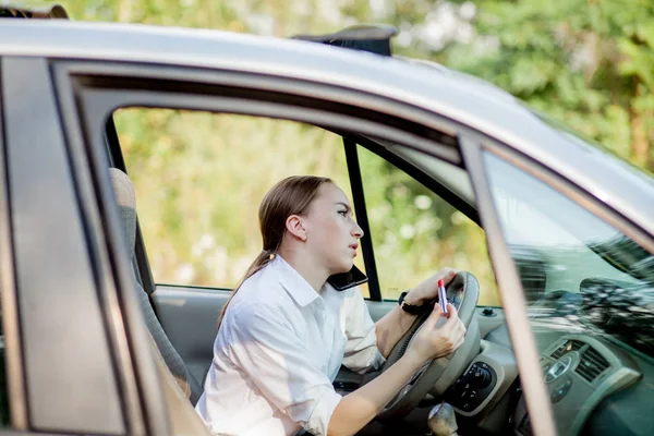 Фотографія молодої бізнес-леді розмовляє по телефону і робить макіяж під час водіння автомобіля в пробці — стокове фото