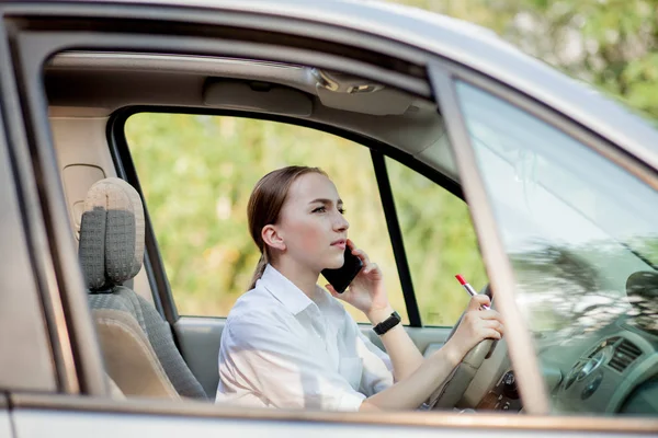 Фотографія молодої бізнес-леді розмовляє по телефону і робить макіяж під час водіння автомобіля в пробці — стокове фото