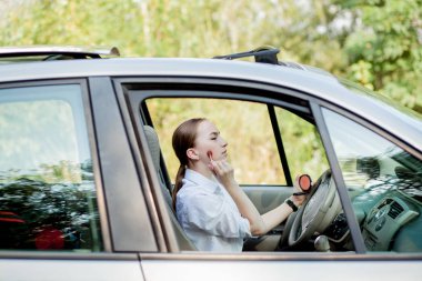 Trafik sıkışıklığında araba sürerken makyaj yapan genç bir iş kadını resmi