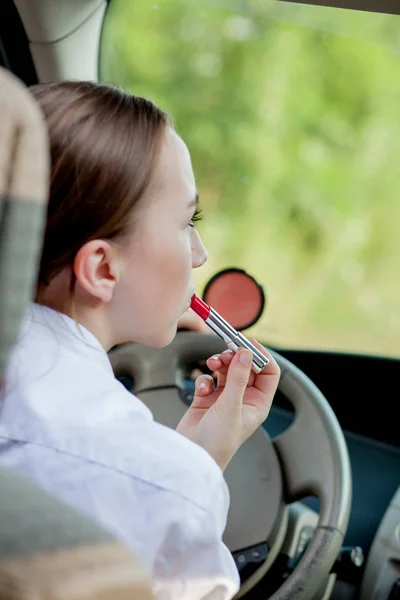 Концепція небезпечного водіння. Молода жінка водій червоного волосся дівчина-підліток малює губи, використовуючи макіяж під час водіння автомобіля — стокове фото