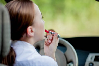 Tehlikeli sürüş kavramı. Genç kadın sürücü, kızıl saçlı genç kız. Dudaklarını boyuyor. Arabayı sürerken makyaj yapıyor.