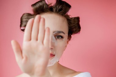 Yüzüne dokunmadan bir maske ve curlers ile güzel genç kız.