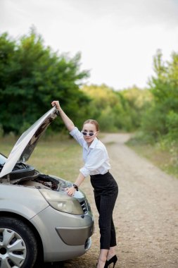 Arabası bozulduktan sonra yol kenarındaki genç kadın hasarı görmek için kaputu açtı.