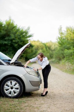 Arabası bozulduktan sonra yol kenarındaki genç kadın hasarı görmek için kaputu açtı.
