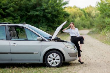 Arabası bozulduktan sonra yol kenarındaki genç kadın hasarı görmek için kaputu açtı.