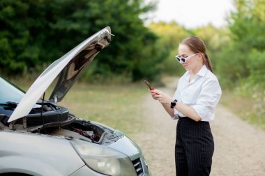 Arabası bozulduktan sonra yol kenarındaki genç kadın hasarı görmek için kaputu açtı.
