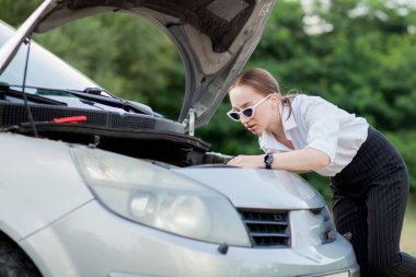 Arabası bozulduktan sonra yol kenarındaki genç kadın hasarı görmek için kaputu açtı.