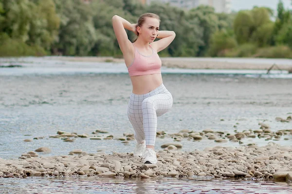 Girl in sports uniforms makes a stretch on the river bank — Stock Photo, Image