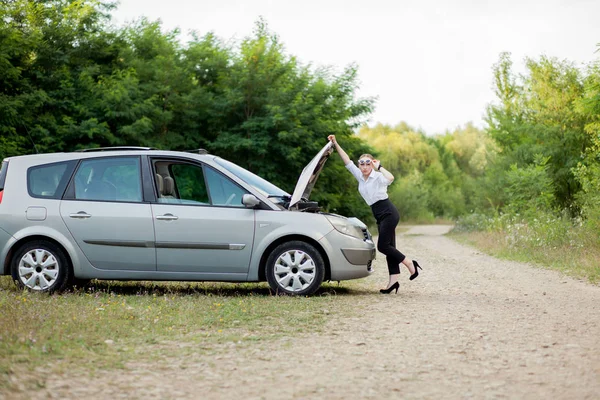 Молода жінка біля узбіччя після того, як її машина зламалася Вона відкрила капот, щоб побачити пошкодження — стокове фото