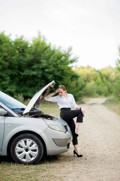 彼女の車が故障した後、道端で若い女性彼女は被害を見るためにフードを開いた — ストック写真