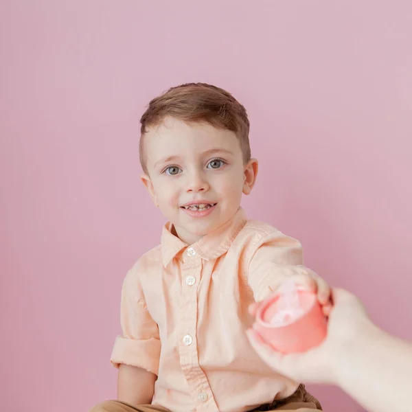 Um rapazinho feliz com um dom. Foto isolada em fundo rosa. Rapaz sorridente segura a caixa de presente. Conceito de feriados e aniversário — Fotografia de Stock