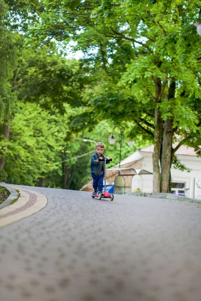 Menino montando scooter no parque da cidade em aummer. Crianças esportes ou — Fotografia de Stock