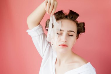 Yüzüne dokunmadan bir maske ve curlers ile güzel genç kız.