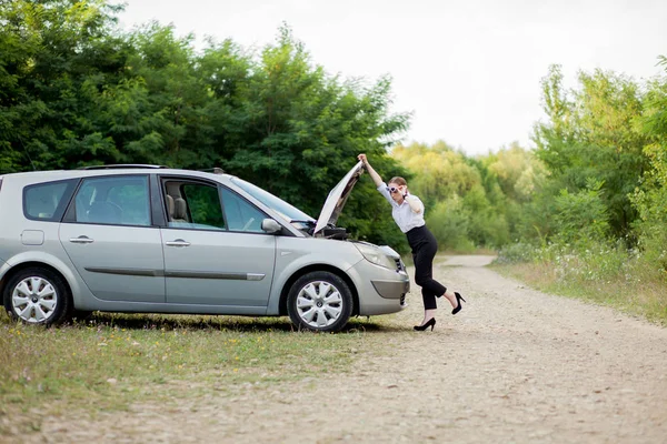Arabası bozulduktan sonra yol kenarındaki genç kadın hasarı görmek için kaputu açtı.
