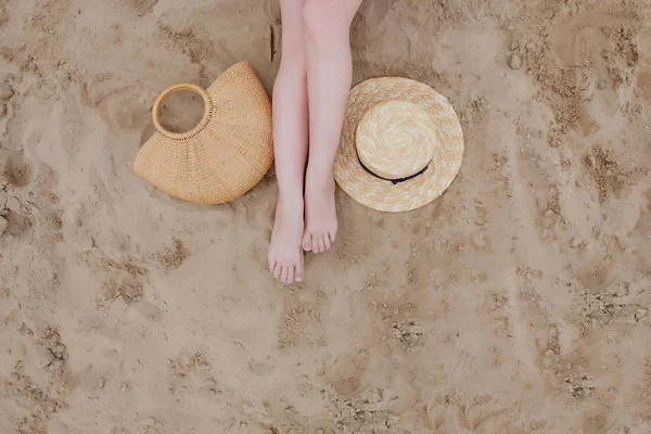 Γυναικεία μαυρισμένα πόδια, ψάθινο καπέλο και τσάντα στην αμμώδη παραλία. Το σχέδιο του ταξιδιού. Χαλαρώστε σε μια παραλία, με τα πόδια σας στην άμμο. — Φωτογραφία Αρχείου
