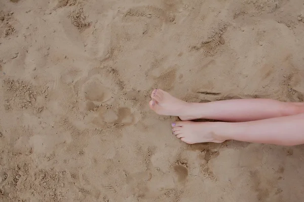 Piernas bronceadas de mujer, sombrero de paja y bolso en playa de arena. Concepto de viaje. Relajarse en una playa, con los pies en la arena . — Foto de Stock