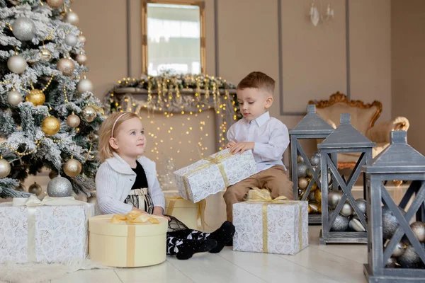 Menina bonito e menino abrindo presentes de Natal. Crianças debaixo da árvore de Natal com caixas de presente. Sala de estar decorada com lareira tradicional. Aconchegante noite quente de inverno em casa — Fotografia de Stock