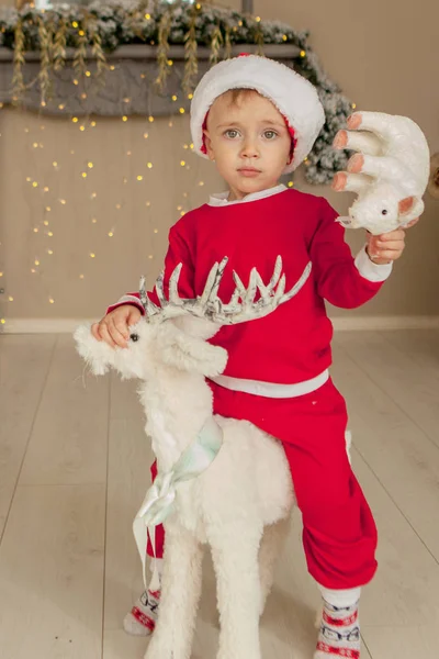 Um rapazinho está à espera do Natal e a divertir-se. o menino está montando um veado de brinquedo para o Natal — Fotografia de Stock