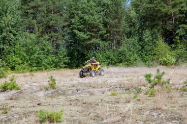 Sarı dörtlü Atv'ye binen adam kumlu bir ormanda tüm arazi aracına biniyor. Ekstrem spor hareketi, macera, turistik.