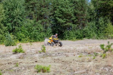 Sarı dörtlü Atv'ye binen adam kumlu bir ormanda tüm arazi aracına biniyor. Ekstrem spor hareketi, macera, turistik.
