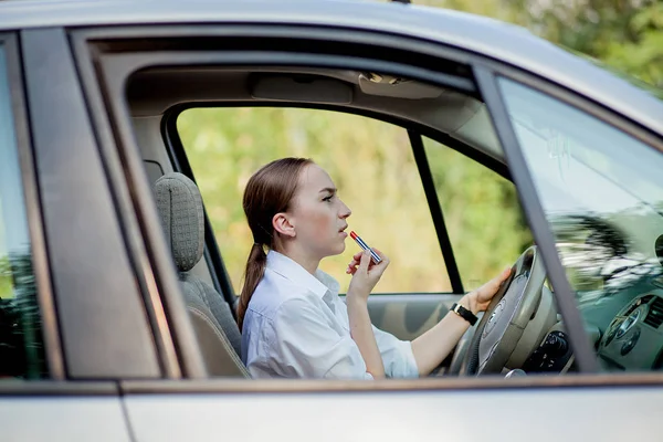 Фотографія молодої бізнес-леді, яка робить макіяж під час водіння автомобіля в пробці — стокове фото