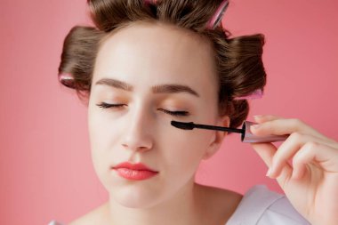 Güzel, neşeli bir genç kız bigudili kız kaşlarını boyuyor. 