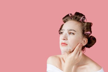 Yüzüne dokunmadan bir maske ve curlers ile güzel genç kız.