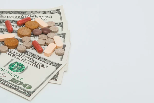 Кольорові лікувальні таблетки та американські долари на білому фоні — стокове фото