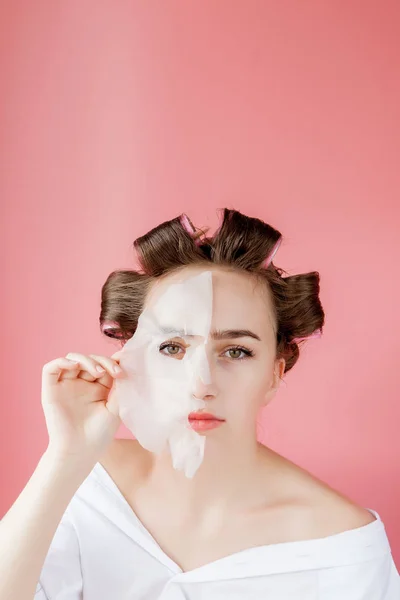 Mooi jong meisje met een masker en krulspelden die haar gezicht aanraken. — Stockfoto