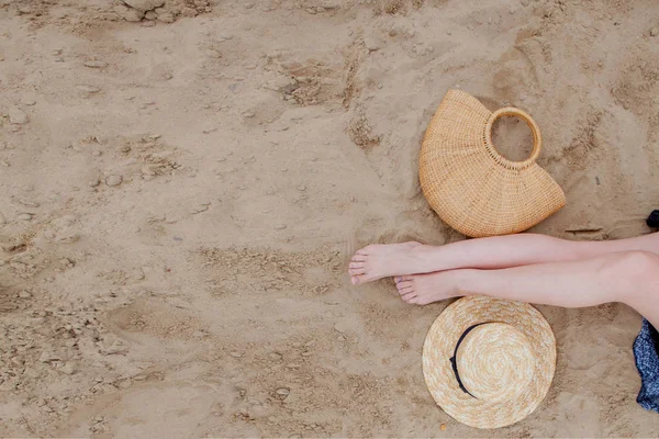 Γυναικεία μαυρισμένα πόδια, ψάθινο καπέλο και τσάντα στην αμμώδη παραλία. Ταξίδια — Φωτογραφία Αρχείου