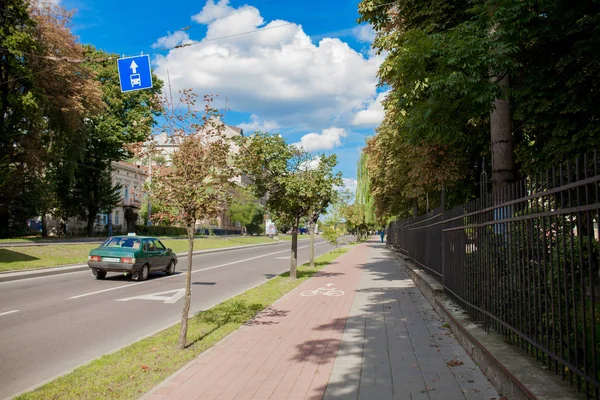 Şehir caddesinde park yolu ve kaldırım arasında korunan bisiklet yolu. Bisikletçiler güzel bahar gününde gidip.