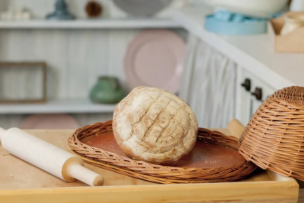 Хлеб возле плетеной корзины на столе в деревенской кухне. Комп — стоковое фото