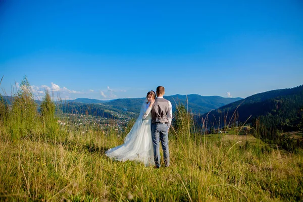 Les jeunes mariés sourient et s'embrassent dans la prairie au sommet de la montagne. Promenade de mariage dans les bois dans les montagnes, les émotions douces du couple, photo pour la Saint-Valentin — Photo