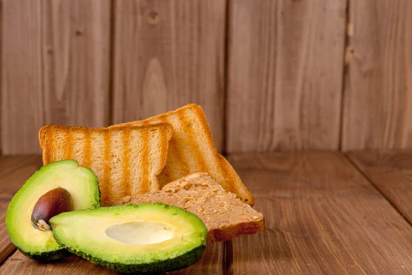 Aguacates y tostadoras con pasta de maní sobre un fondo de madera. Tostadas caseras de desayuno deliciosas y saludables — Foto de Stock