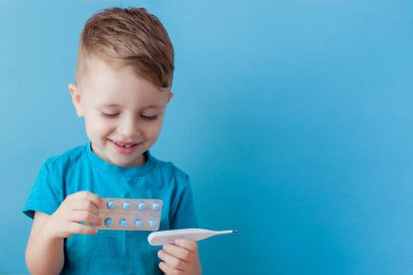 Termometresi olan hasta bir çocuk ateşinin yüksekliğini ölçüyor ve kameraya bakıyor.