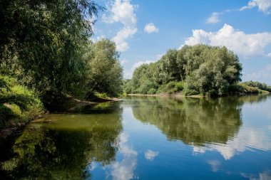 Nehrin arka planına karşı mavi güzel gökyüzü. Bulutlar sakin suda görüntülenir. Ufukta, Dinyester'In yeşil kıyısı, balık avlama yeri