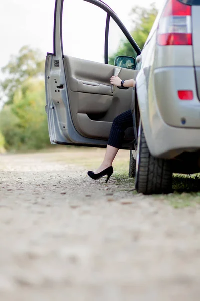 Pebisnis wanita yang berpose di dekat mobil putih dan menunjukkan kaki ramping dan ramping di dekat mobilnya. Wanita sukses dengan rok abu-abu berpose dengan sepatu hak tinggi merah muda — Stok Foto