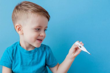 Termometresi olan hasta bir çocuk ateşinin yüksekliğini ölçüyor ve kameraya bakıyor.