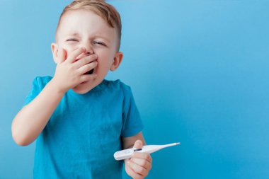 Termometresi olan hasta bir çocuk ateşinin yüksekliğini ölçüyor ve kameraya bakıyor.