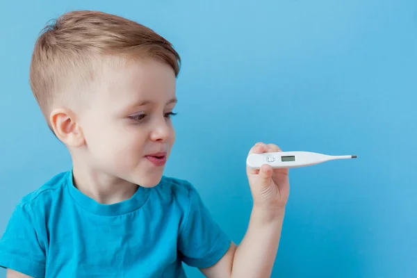 Malo niño pequeño con un termómetro, midiendo la altura de su fiebre y mirando a la cámara —  Fotos de Stock