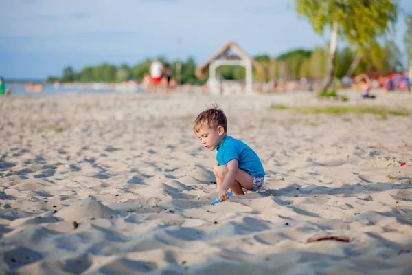 Rapaz a brincar na praia. Criança brinca no mar em férias em família de verão. Brinquedos de areia e água, proteção solar para crianças pequenas. Menino cavando areia, construindo castelo na costa do oceano. — Fotografia de Stock
