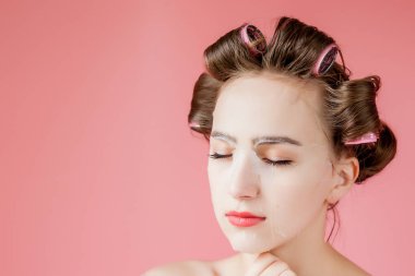 Yüzüne dokunmadan bir maske ve curlers ile güzel genç kız.
