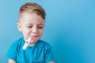 Termometresi olan hasta bir çocuk ateşinin yüksekliğini ölçüyor ve kameraya bakıyor.