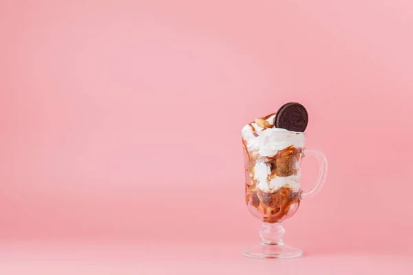 Солодкий десерт у склянці з печивом та збитими вершками на рожевому фоні, селективний фокус та порожній простір — стокове фото