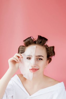Yüzüne dokunmadan bir maske ve curlers ile güzel genç kız.